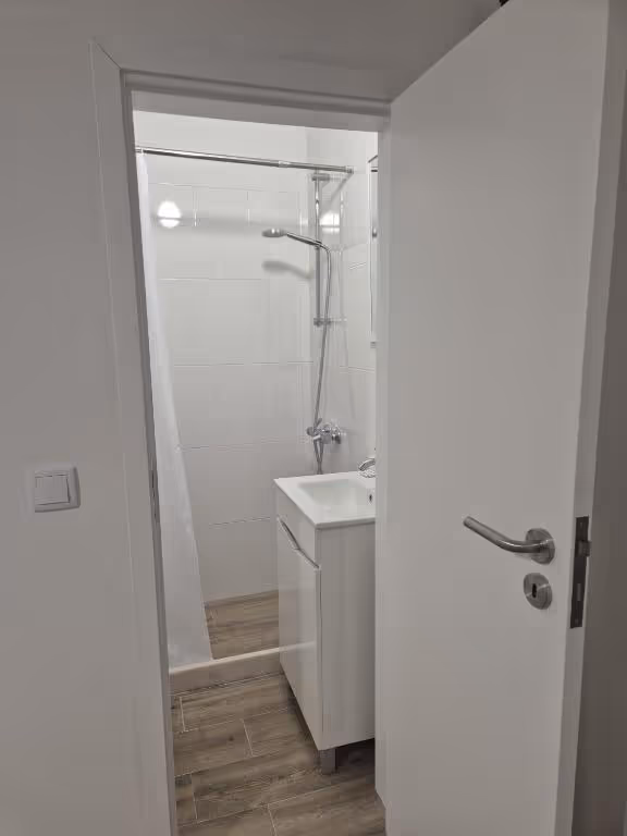 Duche com chuveiro de coluna e lavatório, visto da porta.