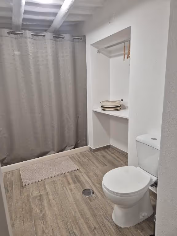 Casa de banho com sanita, cortina de duche e um nicho aberto com toalhas dobradas.