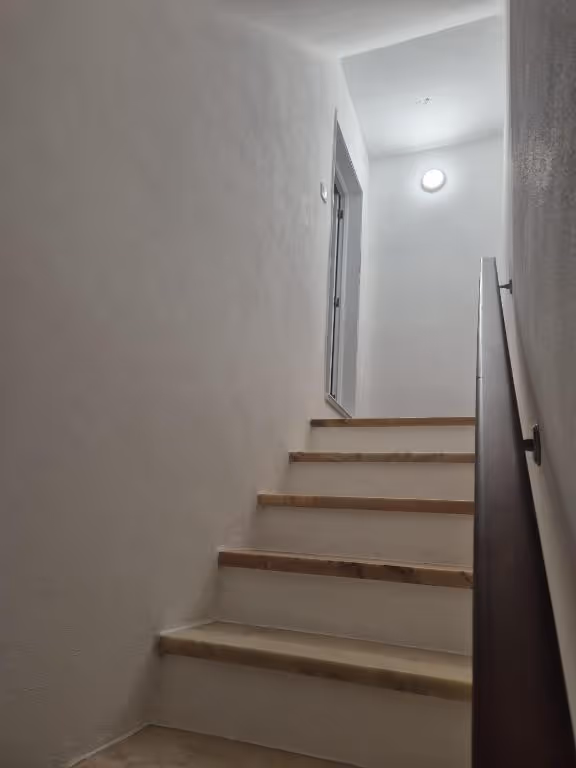 Escada interior de degraus em mármore, com corrimão de madeira e uma janela no patamar.