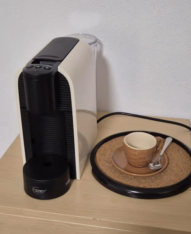 Máquina de café de cápsulas sobre a bancada, com chávena e pires ao lado.
