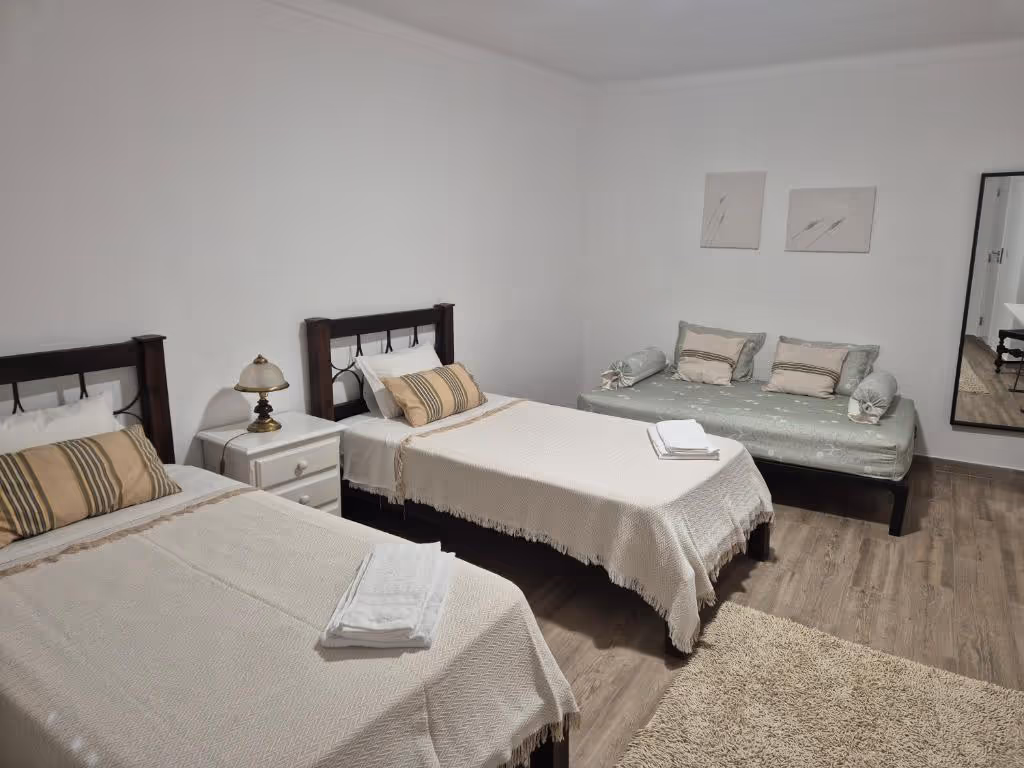 Quarto com duas camas individuais de madeira escura e um sofá-cama junto à parede.