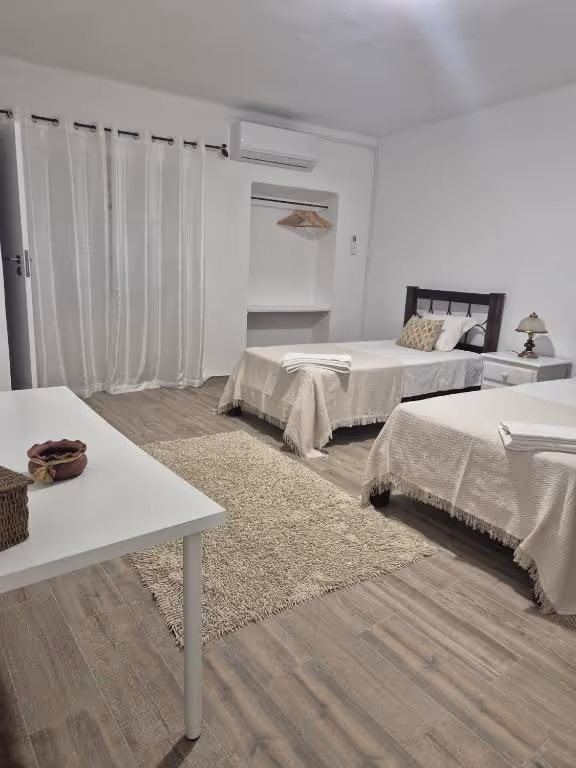 Quarto com duas camas individuais, ar condicionado, cortinados brancos e um nicho com cabides.
