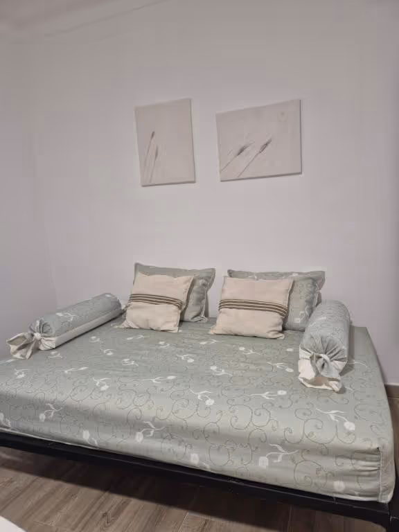 Sofá-cama aberto, feito, com almofadas e dois rolos laterais.