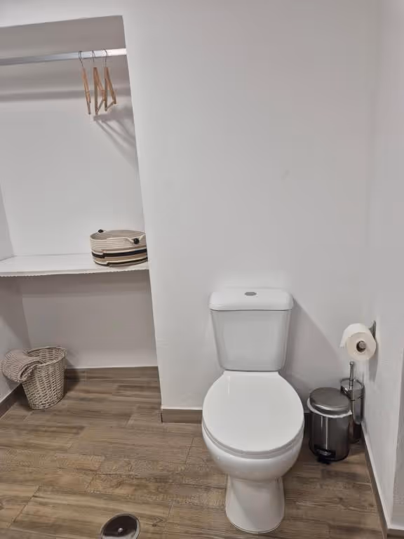 Casa de banho com sanita e um nicho com prateleira, cabides e cesto de vime.